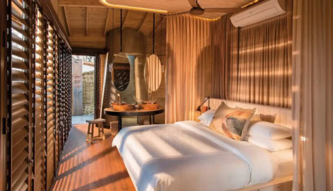 Luxuriöses Schlafzimmer der Sandibe Okavango Safari Lodge mit warmem Holzdesign und großen Fenstern.