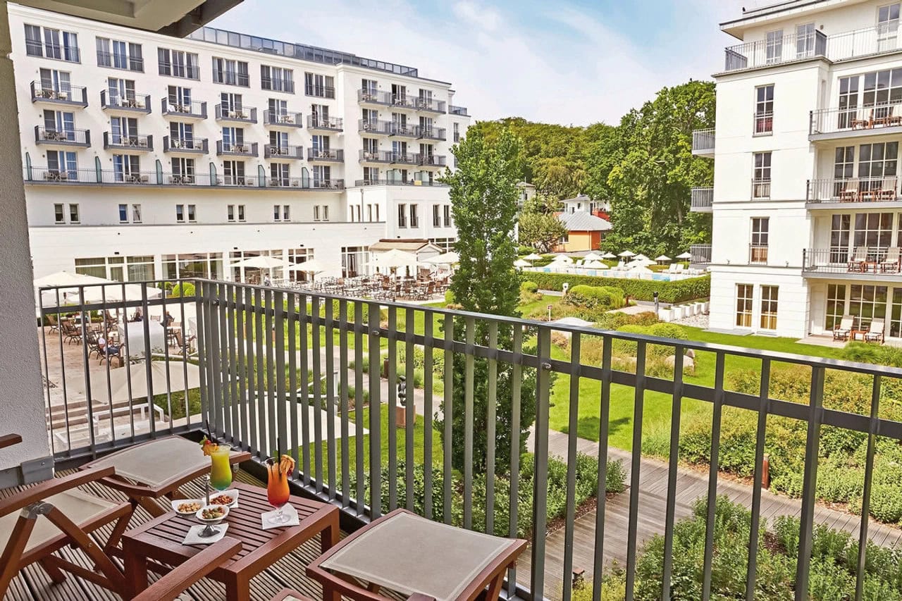 Blick vom Balkon des Steigenberger Grandhotel & Spa Heringsdorf auf die gepflegte Gartenanlage, helle Hotelfassaden, Poolbereich und begrünte Wege