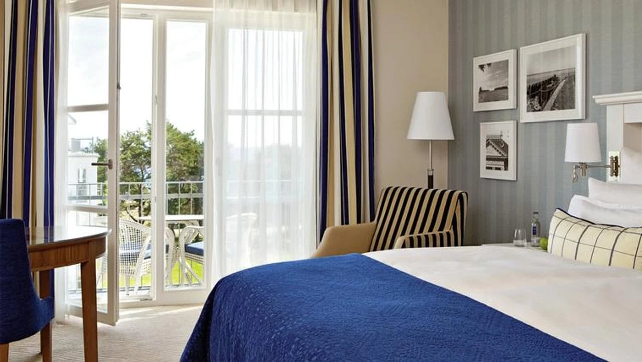 Maritim eingerichtetes Doppelzimmer im Steigenberger Grandhotel & Spa Heringsdorf mit blauem Bettüberwurf, gestreiftem Sessel und französischem Balkon