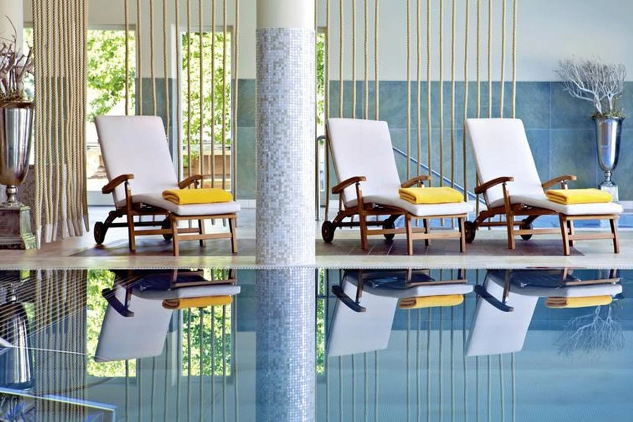 Ruhiger Indoor-Pool im Steigenberger Grandhotel & Spa Heringsdorf mit weißen Liegen, gelben Handtüchern, Spiegelungen im Wasser und hellem Wellnessambiente