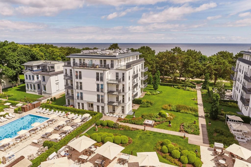 Luftansicht des Steigenberger Grandhotel & Spa Heringsdorf mit Pool, Gartenanlage, hellen Hotelgebäuden, grüner Umgebung und Blick bis zur Ostsee