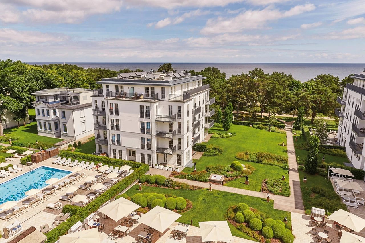Luftansicht des Steigenberger Grandhotel & Spa Heringsdorf mit Pool, Gartenanlage, hellen Hotelgebäuden, grüner Umgebung und Blick bis zur Ostsee