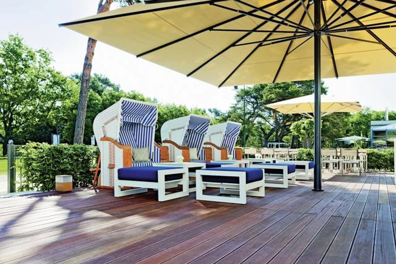 Terrasse im Steigenberger Grandhotel & Spa Heringsdorf mit blau-weißen Strandkörben, großen Sonnenschirmen, Holzboden und grüner Umgebung