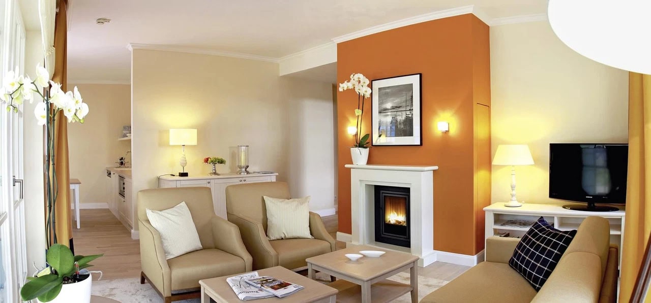 Heller Wohnbereich im Steigenberger Grandhotel & Spa Heringsdorf mit bequemen Sesseln, Sofa, Kamin, Orchidee und warmen Orange- und Cremetönen