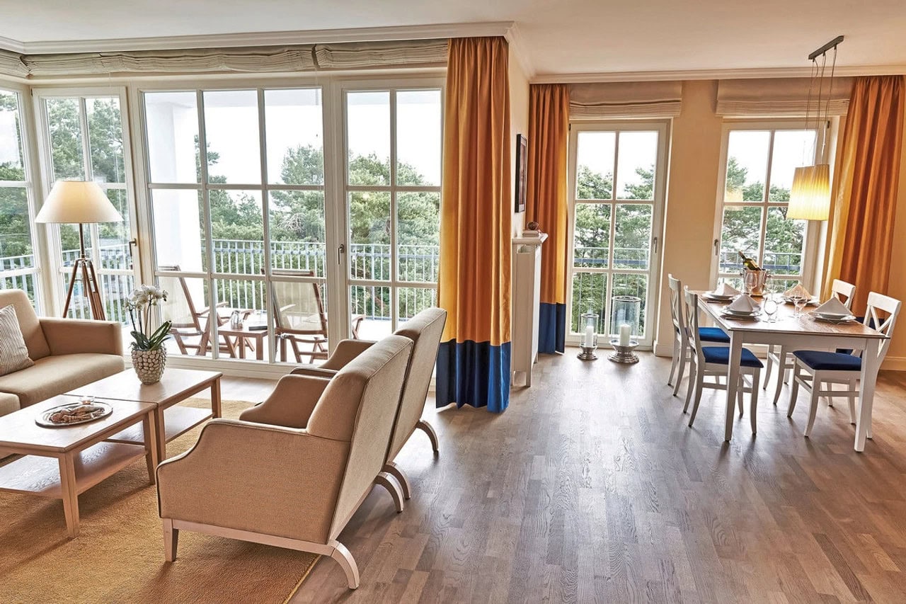 Großzügiger Wohn- und Essbereich im Steigenberger Grandhotel & Spa Heringsdorf mit hellen Sitzmöbeln, Esstisch, großen Fenstern und Balkonblick ins Grüne