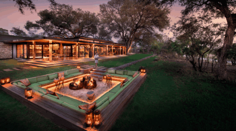 Außenlounge mit Feuerstelle, Sitzgruppen und Blick in die Savanne bei Sonnenuntergang