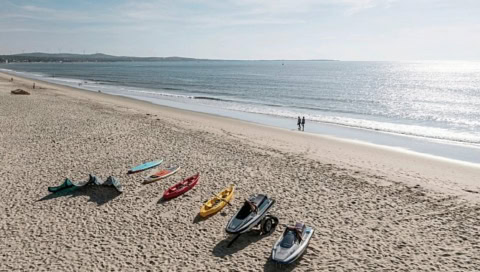 Weitläufiger Sandstrand mit Kajaks und Surfbrettern am Ufer
