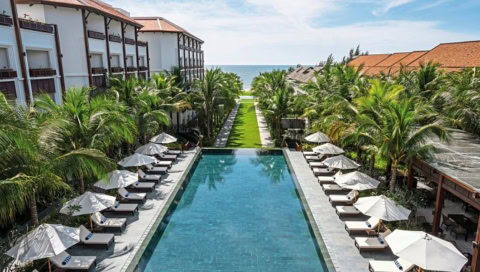 Großer rechteckiger Pool zwischen Hotelgebäuden, gesäumt von weißen Sonnenschirmen