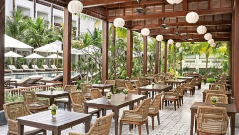 Überdachte Außenterrasse mit Holztischen und Blick auf den Pool