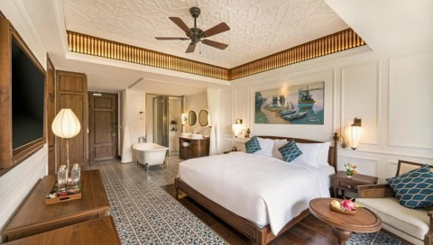 Helles Hotelzimmer mit Doppelbett, Sofa und offener Badewanne im Hintergrund