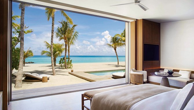 Schlafbereich der Beach Pool Villa mit bodentiefer Fensterfront und Blick auf weißen Sandstrand und türkisfarbene Lagune