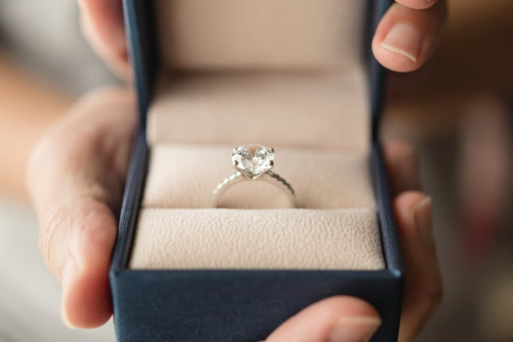 Ein Verlobungsring mit klarem Edelstein steckt in einer beige ausgekleideten Ringschachtel.