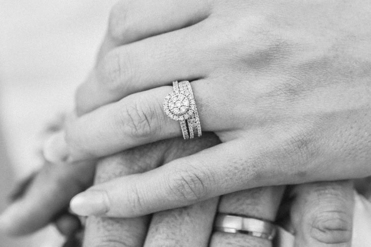 Frauenhand liegt auf der Hand ihres Mannes. Fokus des Bildes ist der Verlobungsring. Schwarzweiß Bild.